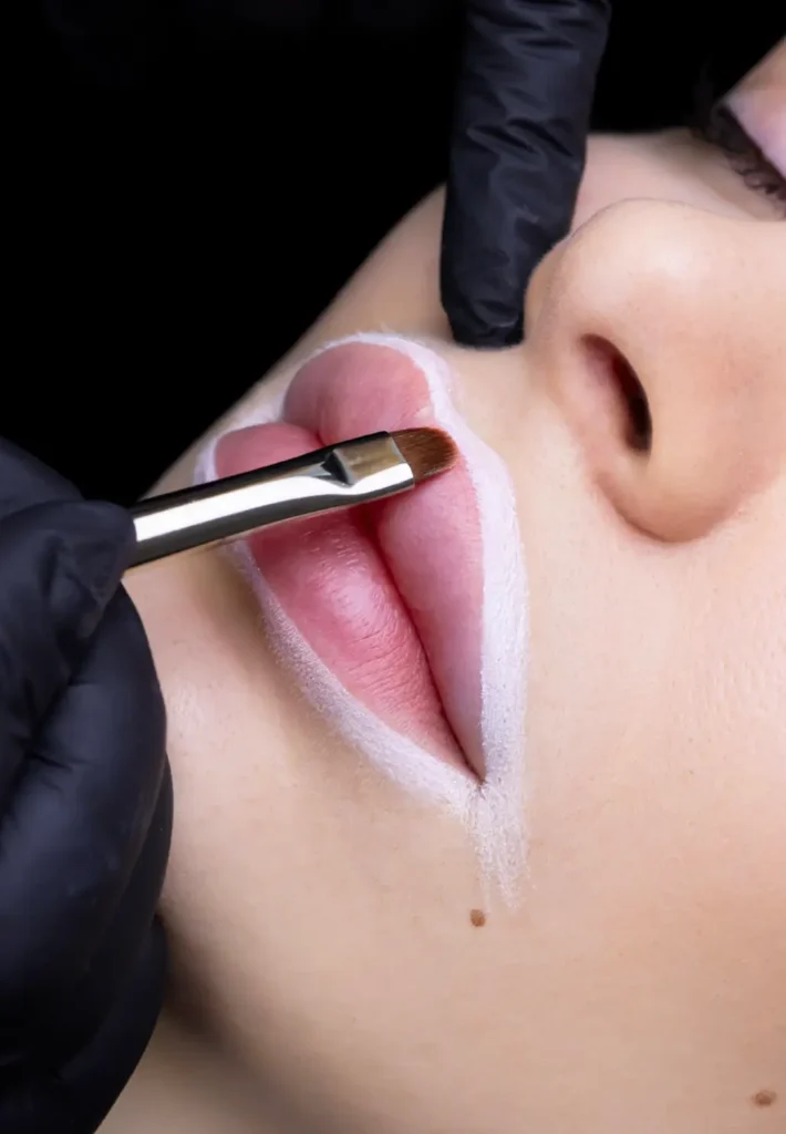 A close view of lip makeup application, outlining the lips with a white cosmetic pencil.