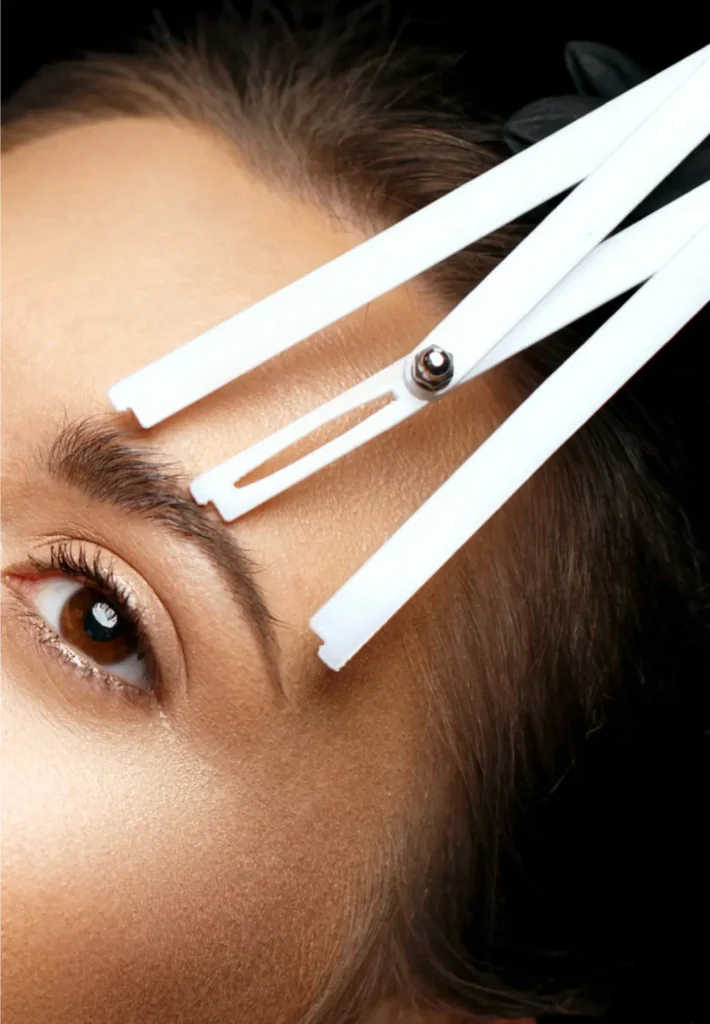 A person's eyebrow being measured and shaped with white mapping tools.